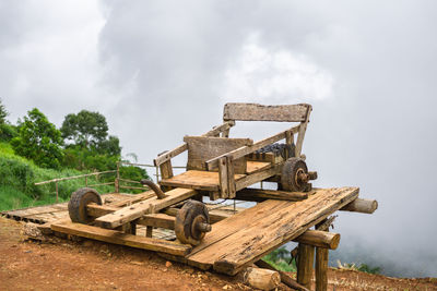 Old wooden bench on field against sky