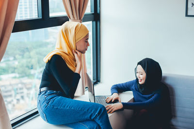 Young woman sitting on window at home