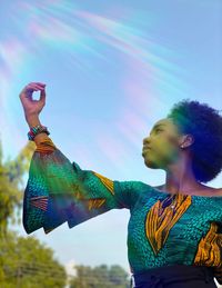 Low angle view of woman holding multi colored umbrella against sky