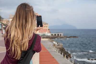 Rear view of woman with ombre hair photographing sea with cellphone