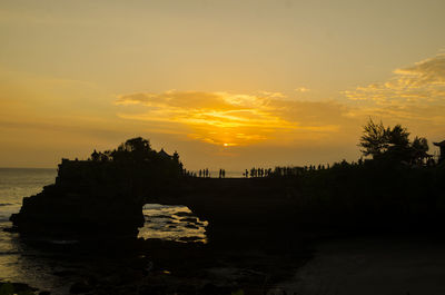 Silhouette rocks by sea against sky during sunset