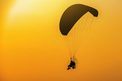 Silhouette person paragliding against orange sky