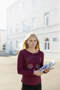 Portrait of teenage girl holding books outdoors