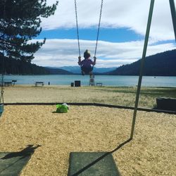 Rear view of  small child on swing on beach with lake against sky