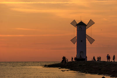 Lighthouse on beach by sea against sky during sunset