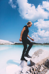 Man standing on rock by lake against sky