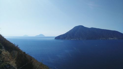 Scenic view of sea and mountains against clear blue sky