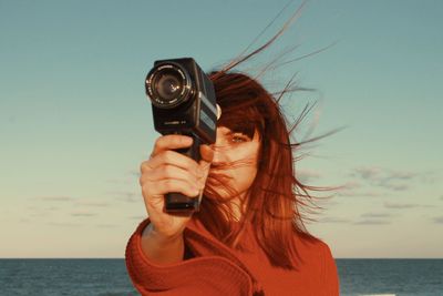 Portrait of woman photographing sea against sky