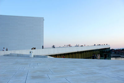 People walking on modern building against clear sky