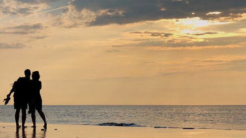 Men standing on beach against sky during sunset