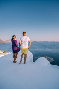 Rear view of people standing on sea shore against clear sky