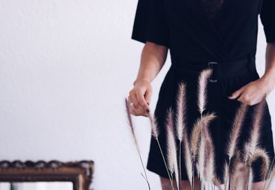 Midsection of woman holding grass while standing against white wall