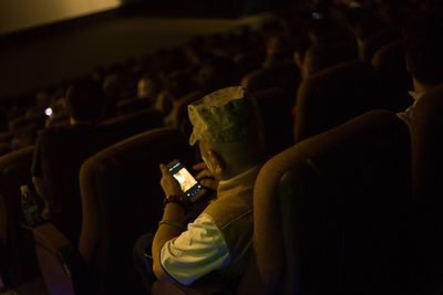 High angle view of man using mobile phone while sitting on seat in theater