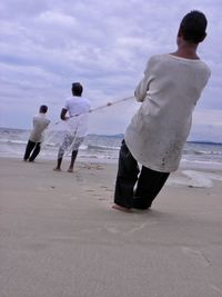 Rear view of boys playing on beach against sky