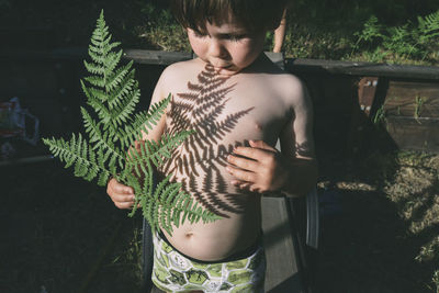 Shirtless boy playing with leaves shadow at backyard