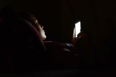 Side view of woman using phone while lying in darkroom