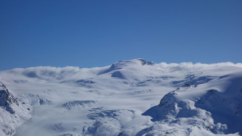 Low angle view of snowcapped mountains against clear blue sky