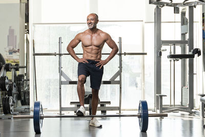 Full length of shirtless man with barbell standing in gym