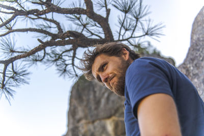 Man in tshirt with beard doing funny face looking down under tree