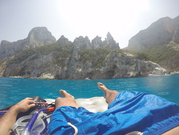 Midsection of person in sea by mountains against sky