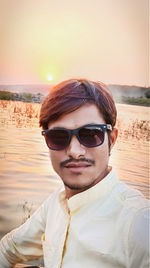 Portrait of young man wearing sunglasses at beach during sunset