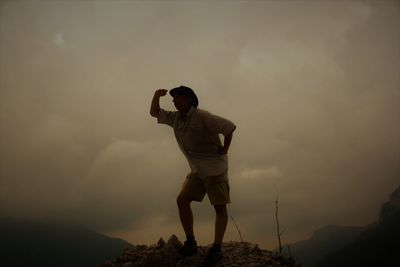 Low angle view of man standing on mountain against cloudy sky during sunset