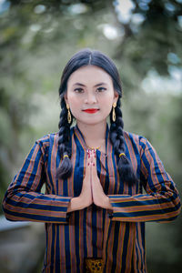 Portrait of young woman standing against trees