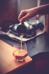 Cropped hand of person pouring drink on table