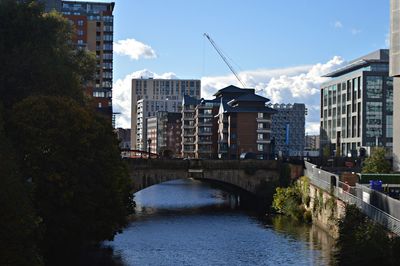 Bridge over river amidst buildings in city against sky