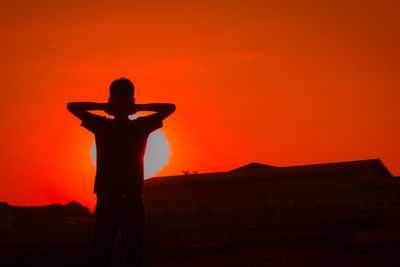 Silhouette man standing on field against orange sky