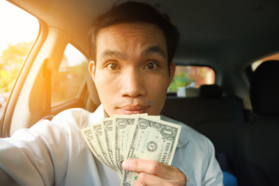 Portrait of mid adult man holding paper currencies while sitting in car