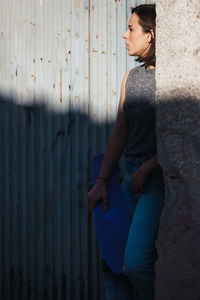 Young woman looking away while standing by corrugated iron