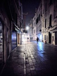 Rear view of person walking on street amidst buildings at night