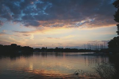 Calm lake with silhouette trees in background at sunset