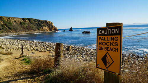 Warning sign on beach against sky