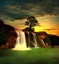 Scenic view of waterfall against sky during sunset