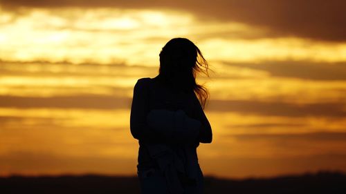 Rear view of silhouette woman standing against orange sky