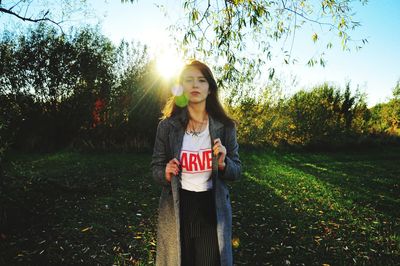 Portrait of young woman standing on field against trees