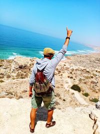 Rear view of man pointing while standing at beach against sky