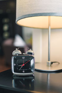 Close-up of alarm clock by illuminated lamp on table