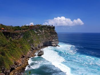 Scenic view of sea by cliff against blue sky
