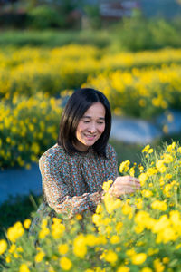 Portrait of smiling young woman with yellow flower in field