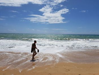 Side view of man walking at beach against blue sky