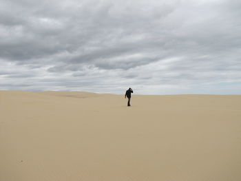 Rear view of man standing in desert against cloudy sky