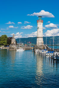 Lighthouse amidst sea and buildings against sky