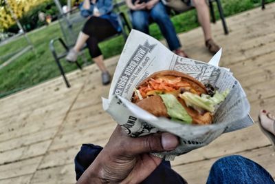 Cropped hand of man holding fresh burger in newspaper at park