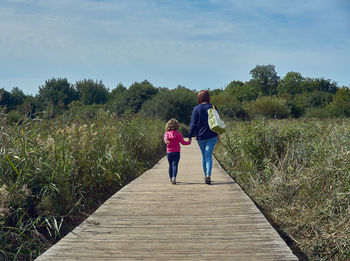 Rear view of woman with daughter walking on boardwalk amidst plants