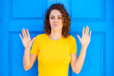 Portrait of smiling young woman gesturing against blue wall