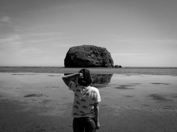 Rear view of boy standing on beach against sky
