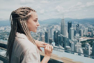 Woman looking at modern buildings in city against sky